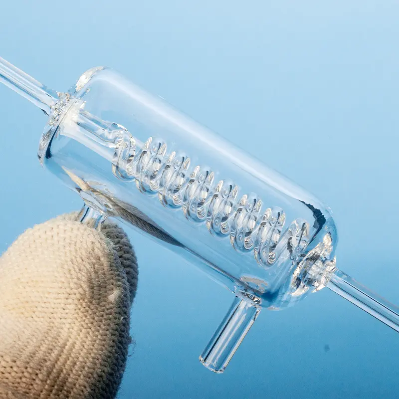 Hand holding a clear quartz glass instrument, likely a compact heat exchanger or condenser, with an internal spiral tube visible.
