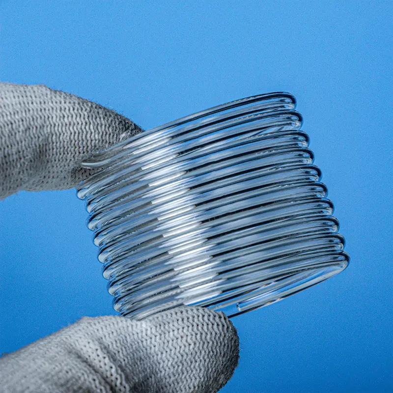 Hand in a protective glove holding a clear, tightly wound quartz glass spiral tube coil.